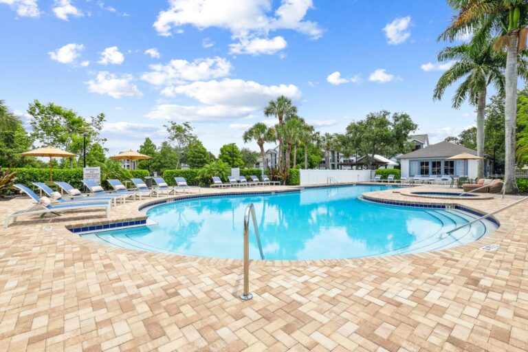 Swimming pool and spa with sundeck and lounge chairs with apartments in background surrounded by native landscaping.