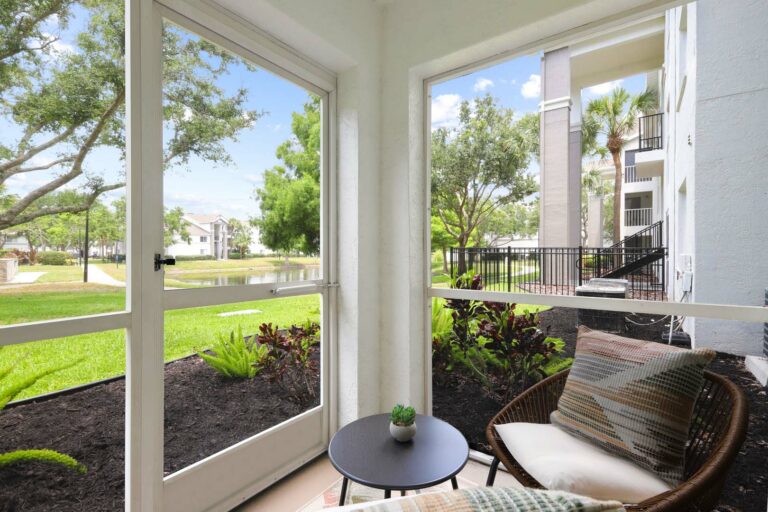Screened in patio with chairs and potted plants overlooking a pond and native landscaping.